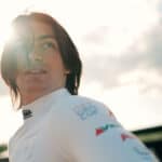 A woman in a white shirt is looking at the sun.
