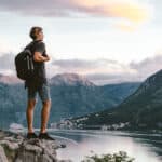 A man standing on top of a mountain, contemplating his purpose as he overlooks a serene lake.