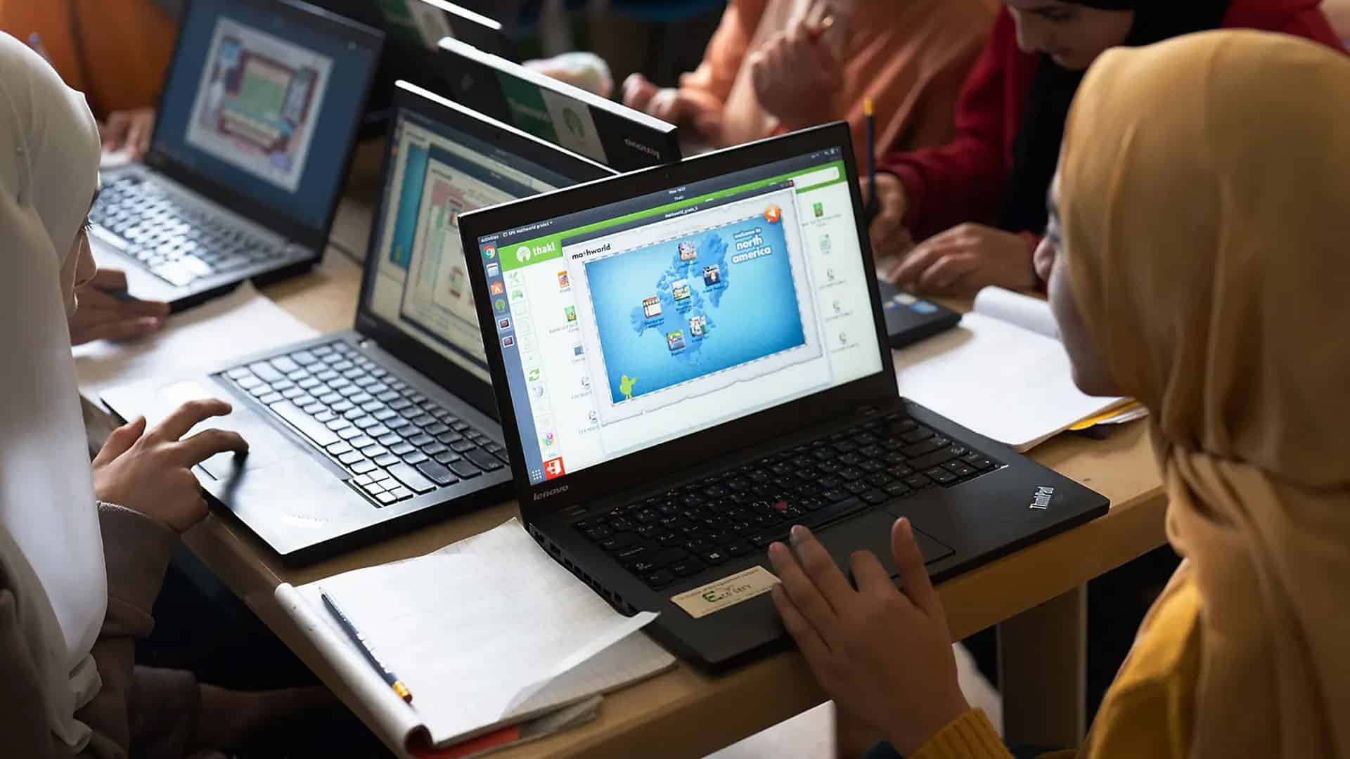 A group of people sitting around a table with laptops.