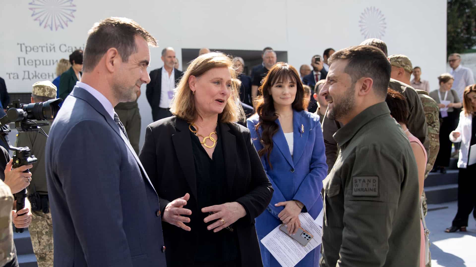 Two men and a woman talking in front of a group of people.